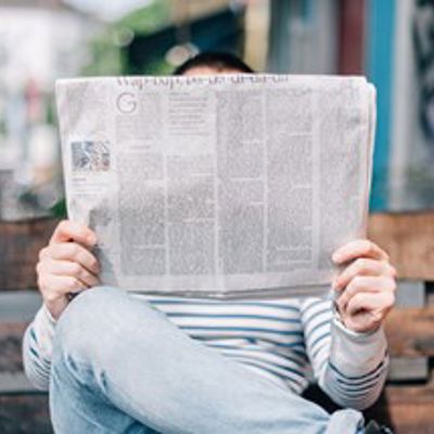 newspaper being held up to cover persons face